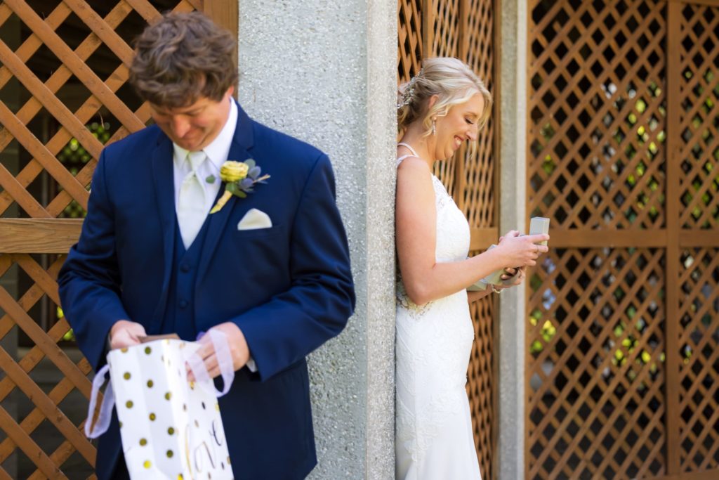 Couple smiles from opposite sides of wall as they open gifts to each other before their Wando River Grill wedding.