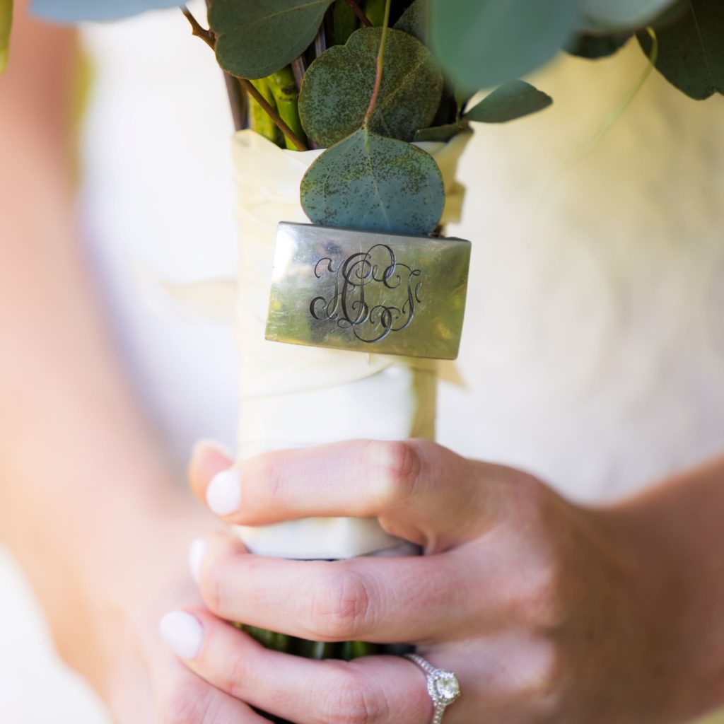 Close up view of a Charleston bride's bouquet accented by her grandfather's monogrammed silver belt buckle at a Wando River Grill wedding.