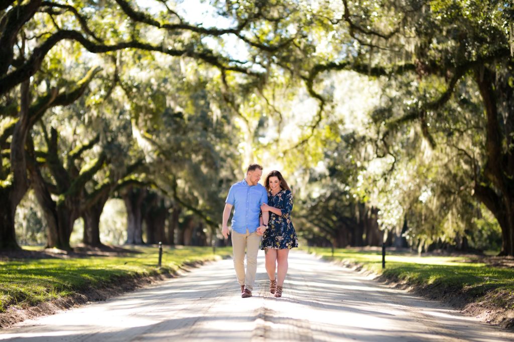A couple strolls down an avenue of oaks in Charleston, South Carolina before a fall wedding in Charleston.